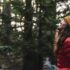 Shauna Doll stands with her winter coat and toque looking up in to the forest canopy, holding her hot drink.