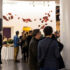 A group of young professionals gather in a large hall conversing with one another, laughing and enjoying beverages.