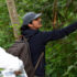 Priya reaches out to touch a plant while a group of people watches.