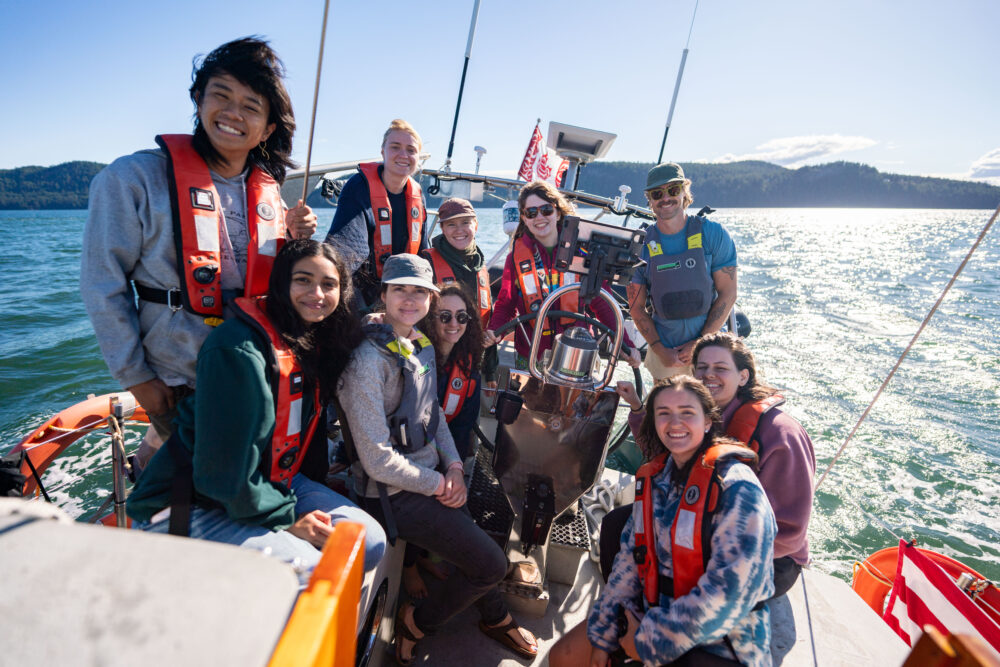 A group of youth sits in the cockpit while sailing