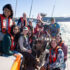 A group of youth sits in the cockpit while sailing