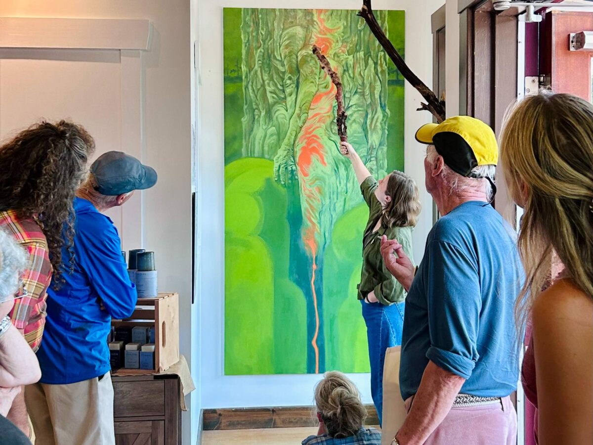 An artist points out features on her mural to a group of people.