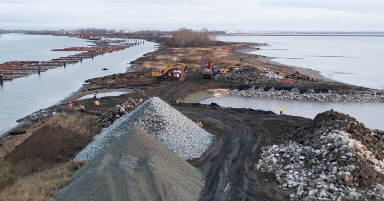 Aerial view of a Fraser River Estuary jetty breach with piles of gravel and excavators and workers on the ground.