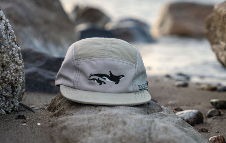 The light green version of the active hat sits on a rocky shoreline, the frothy ocean water inching up towards it.