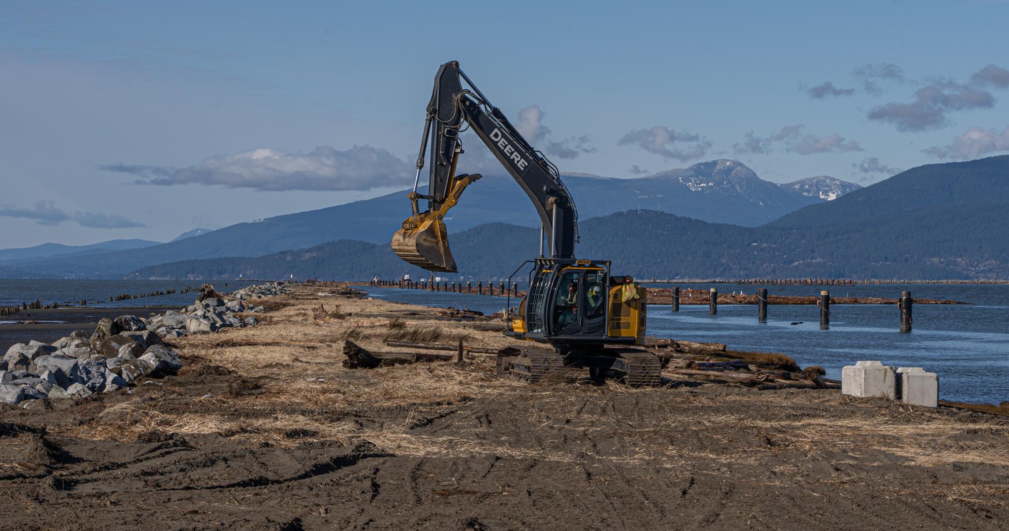 A large piece of machinery scoops dirt on a jetty.
