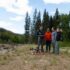 4 people stand outside around a drone near a riverbed.