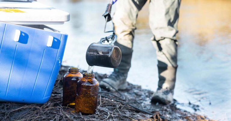 Close up of a person doing a water contaminants sampling with jars and a cooler.