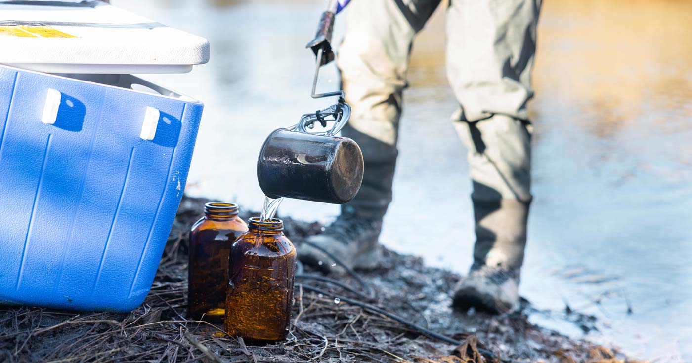 Close up of a person doing a water contaminants sampling with jars and a cooler.