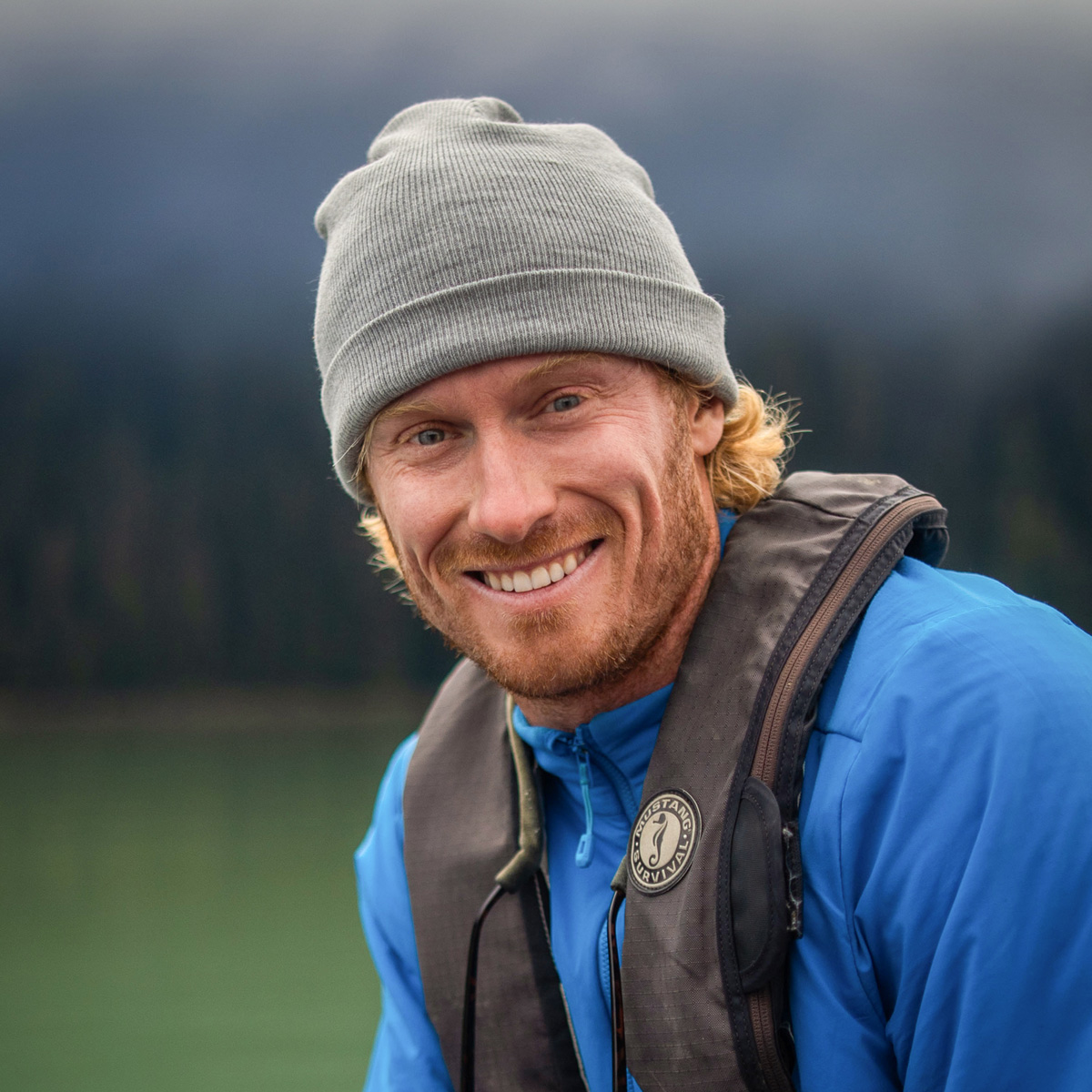 John Kelsey leans over with a life preserver and toque on, smiling warmly, and looking very handsome!