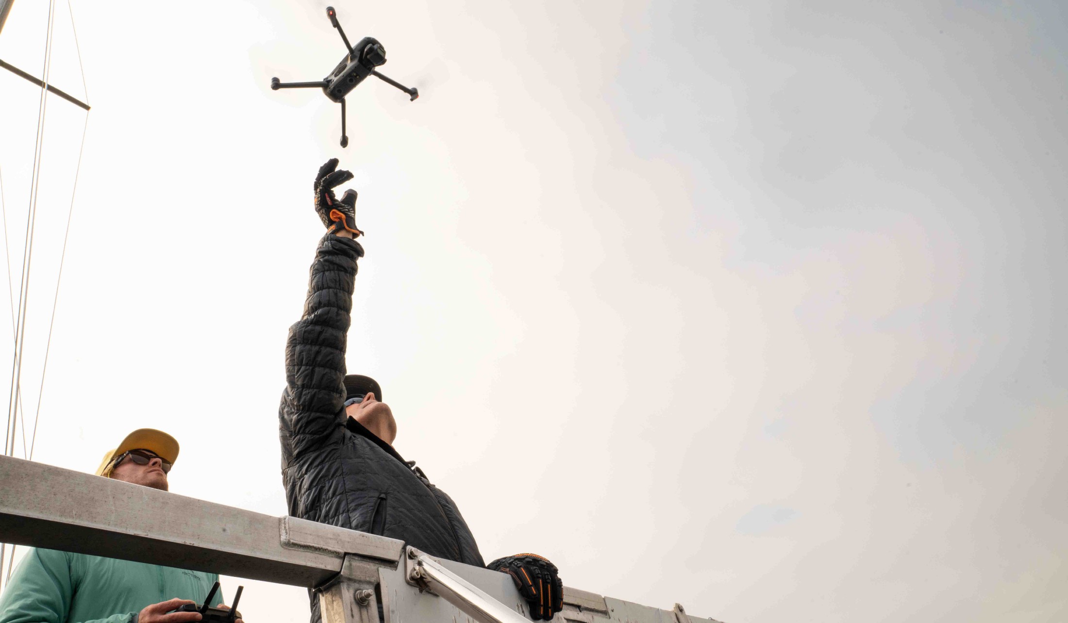 A person in a black jacket releases a drone into the air while someone else stands behind them. 