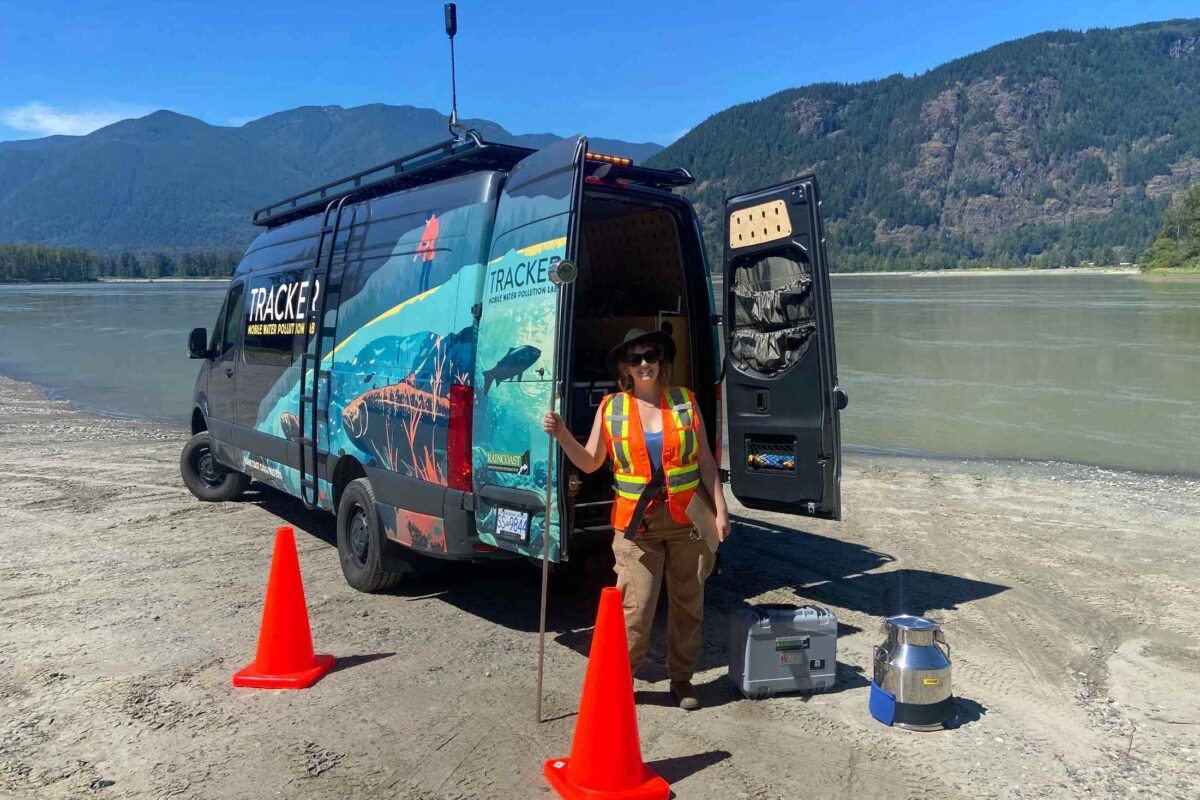 A person wearing an orange safety vest stands in front of our  mobile water pollution lab, Tracker. 