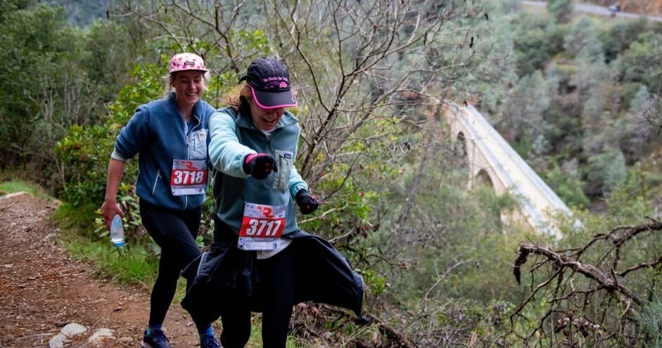 Paige runs behind her mother Erica while they both smile on a trail.