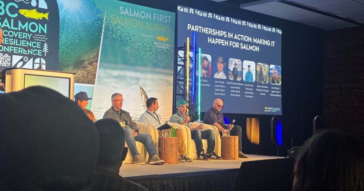 A panel of 5 people sit in chairs on stage a the PSF conference.