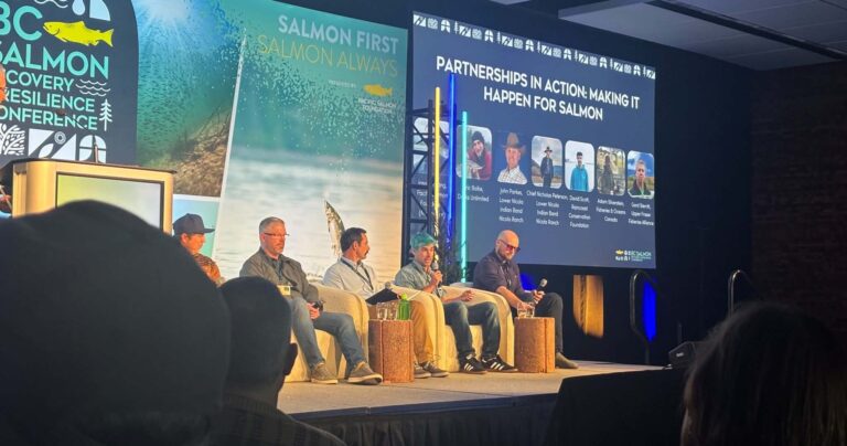 A panel of 5 people sit in chairs on stage a the PSF conference.