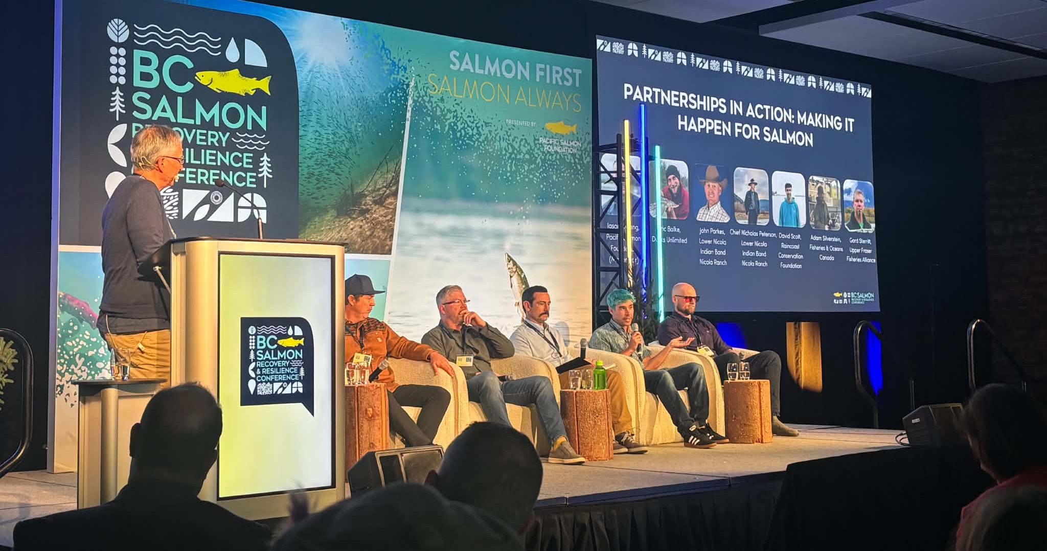 A panel of 5 people sit in chairs on stage a the PSF conference.