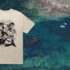 A mockup of a tshirt design is visible over a drone shot of a killer whale swimming through turquoise waters filled with kelp.